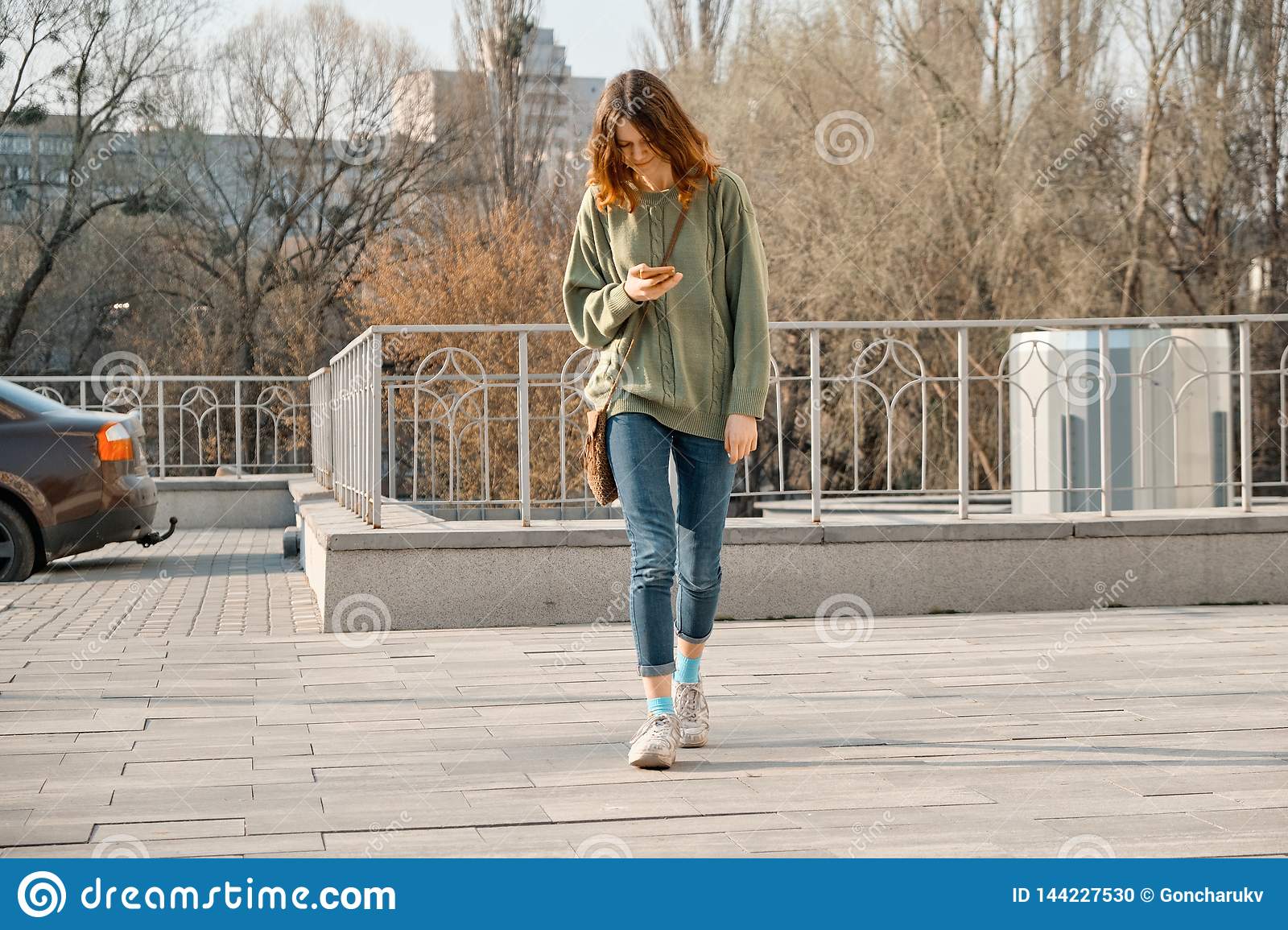 giovane-ragazza-teenager-che-cammina-con-il-telefono-messaggio-di-testo-della-lettura-sullo-smartphone-fondo-giorno-soleggiato-144227530.jpg